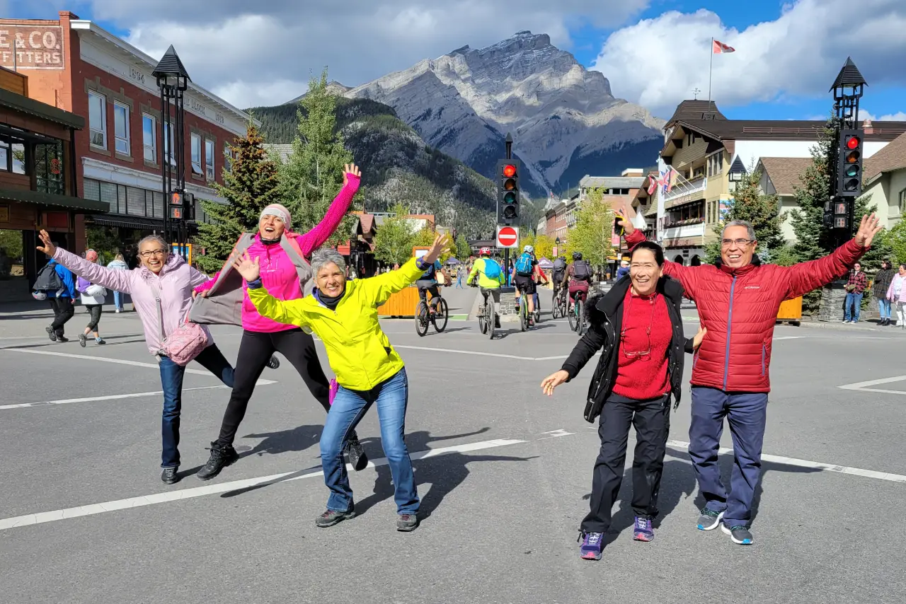 Group of people in colorful jackets posing playfully on a street with mountain backdrop.